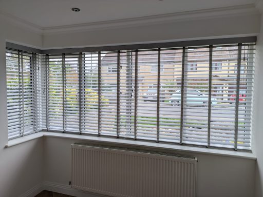 Dark grey faux wood Venetian blinds open in a living room bay window