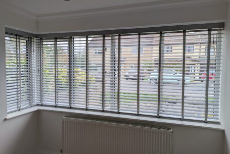 Grey faux wood Venetian blinds with tapes in a living room two sided bay window