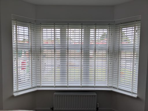 White faux wood Venetian blinds partially open in a bedroom bay