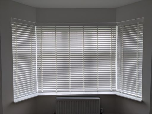 Made to Measure white faux wood closed Venetian blinds with white tapes in a bedroom bay window