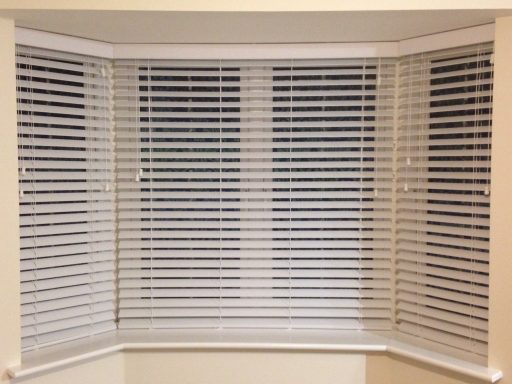 White real wood Venetian blinds partially closed in a living room bay window